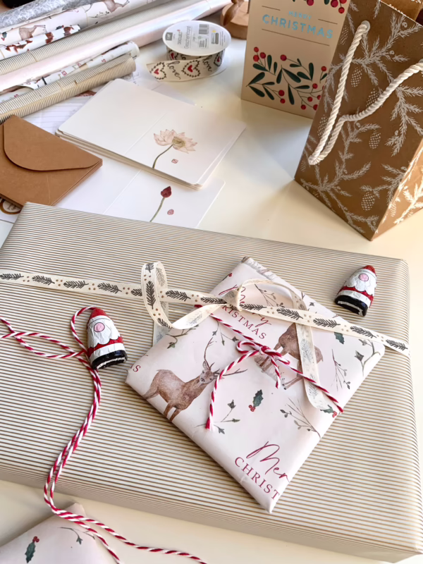 Holiday gift-w wrapping setup with striped and patterned paper, ribbon, and a small wrapped present featuring a botanical card.